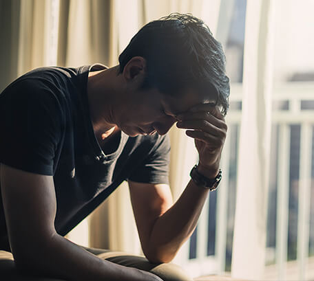 A man with eyes closed and head down holding his head with one hand