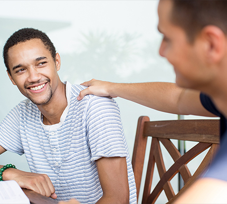 A man touching the shoulder of a young man while talking on a table